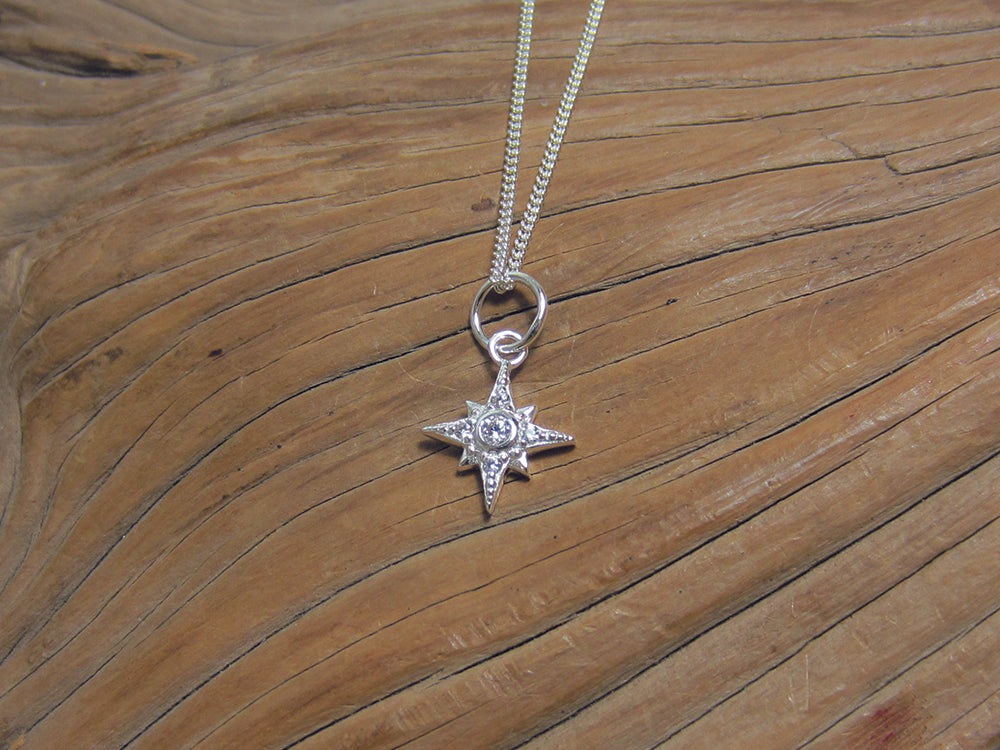 A sparkly little sterling silver star pendant which is set with cubic zirconias and measures about 10mm across. It is shown here on a fine curb chain. 925 Silver Canterbury.